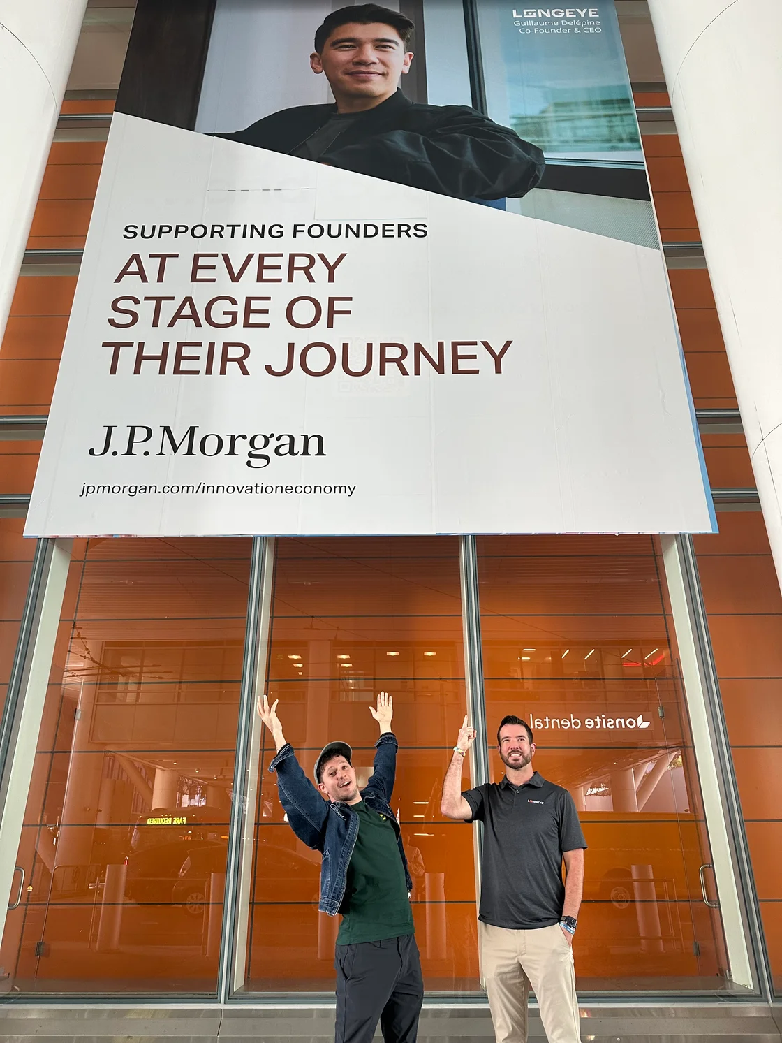 Two Longeye team members posing beneath a large J.P. Morgan billboard featuring Longeye CEO Guillaume Delépine